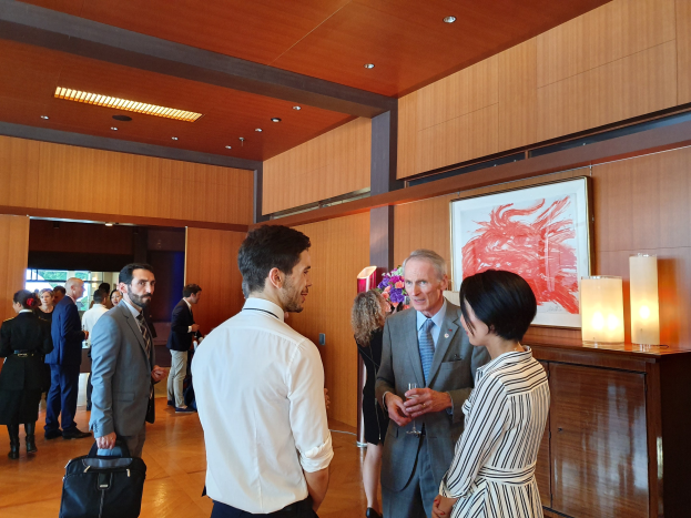 Eine Gruppe von Menschen, die in einem Raum mit einer hölzernen Wand mit einem Fotorahmen und Lampen sprechen, einige halten Taschen auf einer von der Nationalen Kunstgalerie Singapore veranstalteten Kunstmesse.