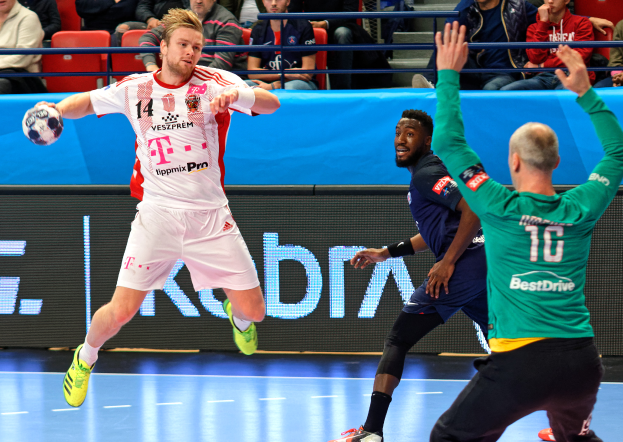 Eine Gruppe von Männern spielt Handball auf einem Court, mit einem Ball in der Mitte der Aktion, während Zuschauer im Hintergrund zusehen. Der Text "Futsal World Cup 2019 - Bayern Munich vs Paris Saint-Germain" ist auf einer Tafel zu sehen.