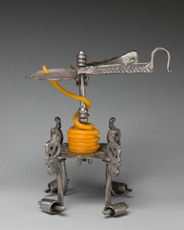 Ein metallener Korkenzieher mit einer hellgelben Feder an seiner Oberseite, der einen zylindrischen Körper, einen Griff auf einer Seite und einen Ausguss auf der anderen Seite hat.