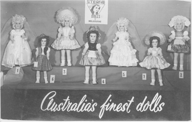 Ein Schwarz-Weiß-Foto einer Reihe australischer Puppen, jeweils mit einzigartigen Outfits und Frisuren, mit einem Plakat im Hintergrund, das Text und ein Logo zeigt.