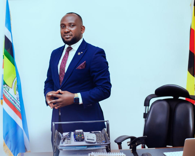 Ein Mann im Anzug steht vor einem Schreibtisch mit Laptop, Telefon, Büchern und Papieren, mit Flaggen an der Wand dahinter und einem Stuhl rechts von ihm, was darauf hindeutet, dass er der neu ernannte Präsident der Republik Zimbabwe ist.