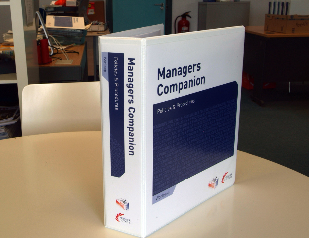 Ein Buch auf einem Tisch mit einem Stuhl dahinter, eine Tür, Feuerlöscher, Akten und andere Gegenstände im Hintergrund.