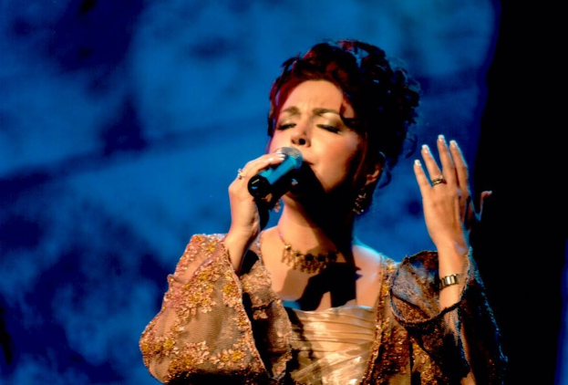 Frau in goldenem Kleid, das Mikrofon haltend, auf der Bühne des Eurovision Song Contest mit blau-schwarzem Hintergrund.