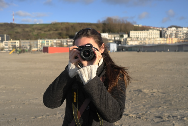 Eine Frau mit einer Kamera vor einigen Gebäuden.