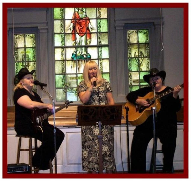 Drei Frauen, eine singt in ein Mikrofon, während die anderen beiden eine Gitarre und ein Mikrofon halten.