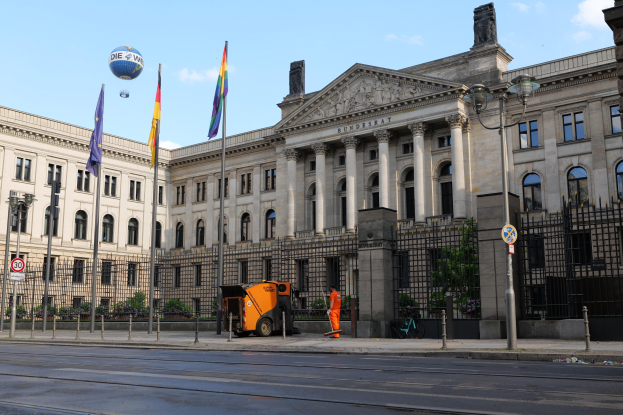 Großes modernes Regierungsgebäude mit zahlreichen Fenstern, als Bundestag in Berlin, Deutschland identifiziert, umgeben von Straßeninfrastruktur und Fußgängern unter einem bewölkten Himmel.