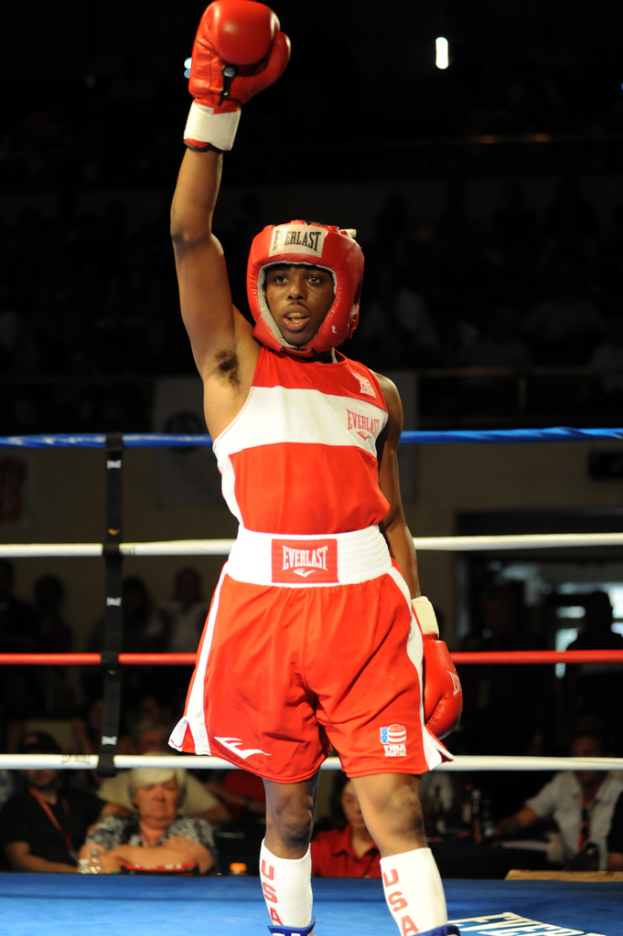 Ein Mann in einem Boxring, der Boxausrüstung, Helm und Handschuhe trägt, mit Zuschauern im Hintergrund.