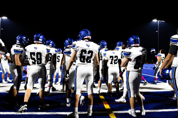 Eine Gruppe von Fußballspielern in Helmen und Stiefeln steht auf einem Feld, mit beleuchteten Lichtmasten im Hintergrund.