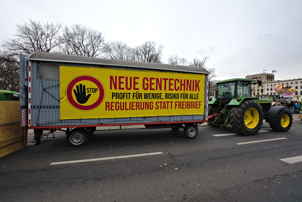 Ein Lastwagen mit einer Tafel fährt auf einer Straße während einer Demonstration in Deutschland, umgeben von Menschen, Bäumen, Gebäuden und einem klaren blauen Himmel.