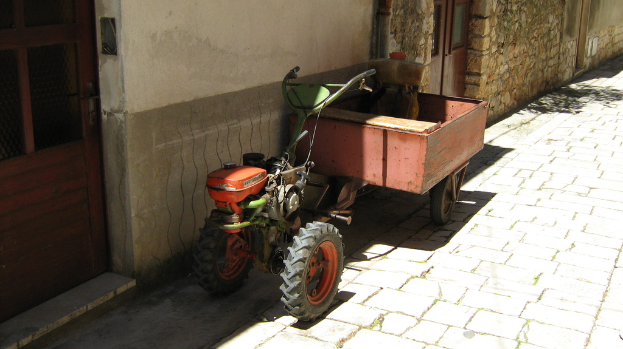 Ein Traktor mit einem Anhänger auf einer Straße, neben einem Haus mit Türen.