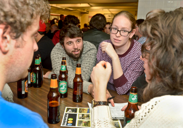 Mehrere Personen auf beiden Seiten eines Tisches mit Bierflaschen, die scheinbar in einer Bar sind.