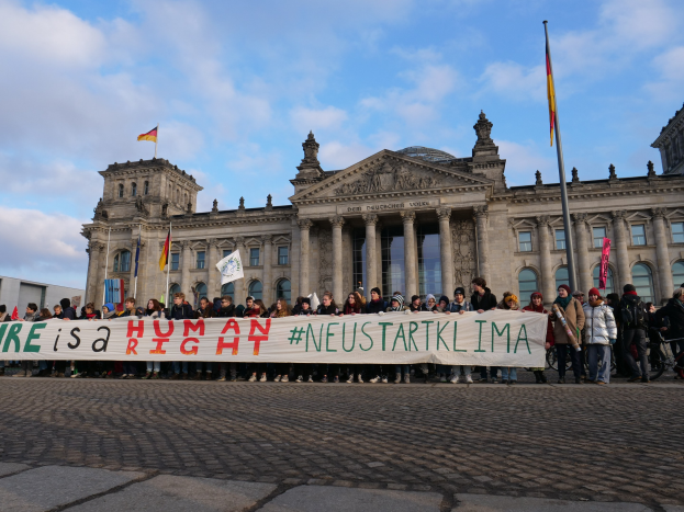 Gruppe von Menschen, die vor dem Reichstag in Berlin stehen und eine Fahne mit der Aufschrift "Wir sind ein Menschenrecht" halten.