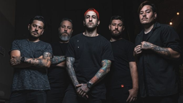 Eine Gruppe von Männern, die in einem dunklen Raum während eines Interviews stehen, von rechts beleuchtet, wahrscheinlich für die Band Avenged Sevenfold.