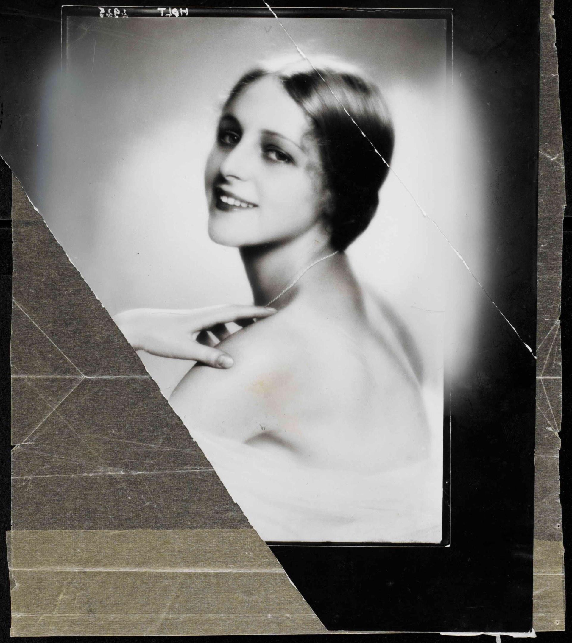 Schwarzes und weißes Foto einer Frau in einem Kleid mit einer 1920er-Jahre-Frisur, die direkt in die Kamera lächelt.