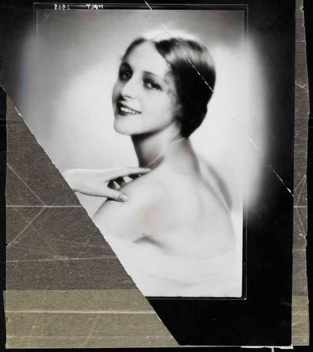 Schwarzes und weißes Foto einer Frau in einem Kleid mit einer 1920er-Jahre-Frisur, die direkt in die Kamera lächelt.