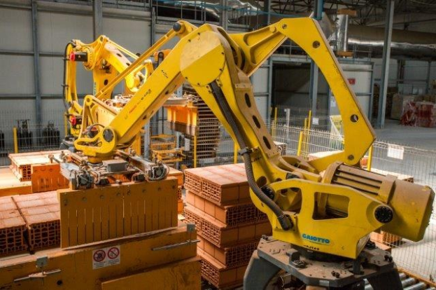 Ein großes Lagerhaus voller numerous boxes, Kräne, einen Zaun, Pfosten und andere industrielle Ausrüstung, mit einer Wand im Hintergrund, die auf eine größere industrielle Umgebung hinweist.