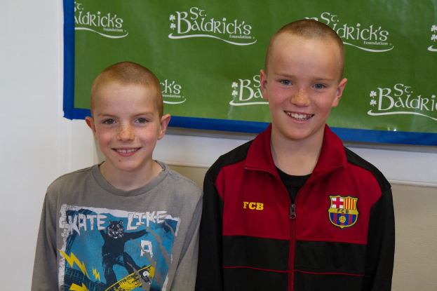 Zwei Jungs nebeneinanderstehend, die lächeln, mit einem Banner im Hintergrund mit Text.