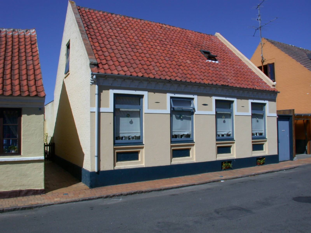 Eine Reihe von Häusern mit roten Dächern und Fenstern entlang einer Straße, mit einer Straße im Vordergrund und einem klaren blauen Himmel im Hintergrund, mit Text, der darauf hinweist, dass sie in den Niederlanden zum Verkauf stehen.