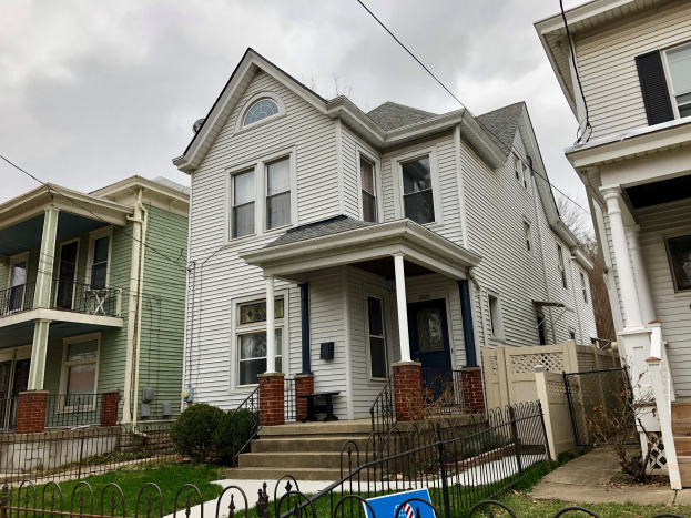 Reihe von Häusern mit Fenstern, Türen, Säulen, Geländern, Stufen und Dächern, umgeben von einem Metallzaun, Gras, Pflanzen, Bäumen und einer bewölkten Himmel, mit einem Mietschild am Boden, das die Adresse 5901 S Elmwood Ave, Chicago 60618 anzeigt.