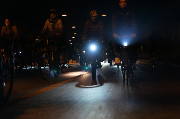 Eine Gruppe von Menschen, die nachts mit Fahrrädern eine Straße entlangfahren, alle tragen Helme.