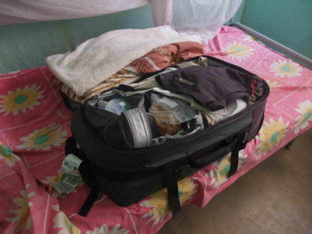 Ein Zelt mit einem Gepäckstück darin, umgeben von Bäumen, mit einem Fahrzeug in der Nähe.