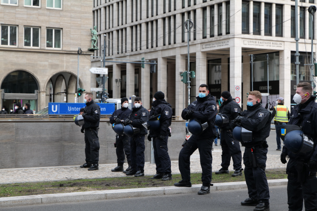 Polizeibeamte in schwarzen Uniformen und Masken stehen vor einem Berliner Gebäude mit Glasfenstern, Säulen und Laternen, einige halten Helme.