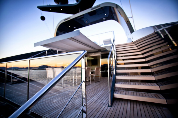 Ein modernes Glasgebäude mit Treppen auf der rechten Seite, Stühle um einen Tisch auf der linken Seite und eine Glasumzäunung unten links.