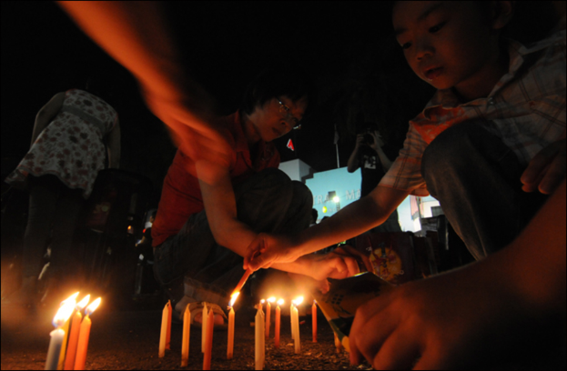 Eine Gruppe von Menschen zündet Kerzen am unteren Bildrand an.