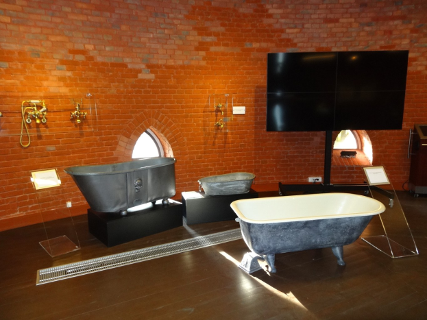 Ein gemütliches Badezimmer mit einer Ziegelwand, einer zentralen Badewanne, an der Wand montierten Wasserhähnen auf der linken Seite und einem an der Wand montierten Fernseher auf der rechten Seite.