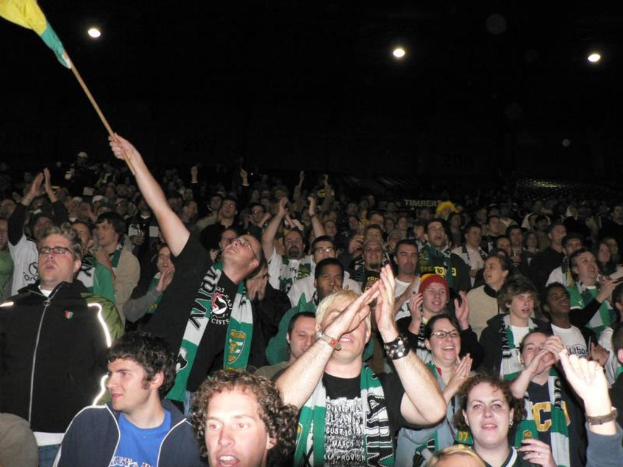 Eine große Menschenmenge versammelt sich, klatscht und amüsiert sich, während eine Person eine Fahne schwenkt.