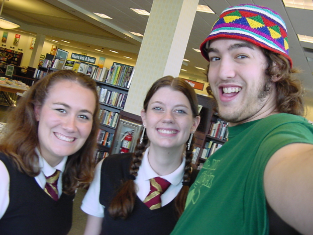 Ein Mann und zwei Studenten machen ein Selfie in einer Bibliothek, mit Bücherregalen voller Bücher im Hintergrund.