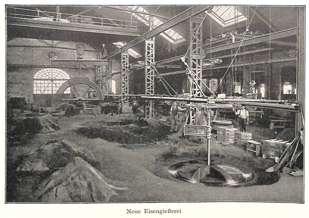 Ein altes Schwarz-Weiß-Foto einer Fabrik mit Arbeitern, die eine Maschine bedienen, umgeben von Metallstangen und -pfosten, mit dem Text "Neue Eisenglebeerei, die erste Fabrik in Deutschland" unten.