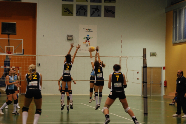 Ein Volleyballspiel in einem Indoor-Court mit einem Basketballkorb im Hintergrund.