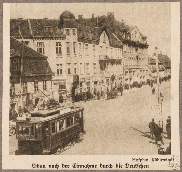 Ein altes Schwarz-Weiß-Foto einer Straßenlandschaft mit einer Tram, Gebäuden, Straßenlaternen, Ampeln und Passanten, mit Text am unteren Rand.