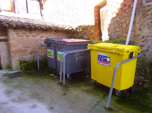 Zwei gelbe und graue Mülltonnen auf Rädern nebeneinander vor einem Gebäude mit einer Wand und einem Fenster im Hintergrund.