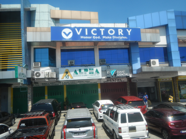 Zahnklinik Victory Dental Clinic in Cebu City, Philippinen, mit Fahrzeugen vor dem Gebäude, einer Person in der Nähe und sichtbaren Texttafeln.