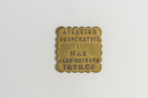 Eine Messingtafel mit der Aufschrift "Luftfahrtkooperative" vor einem weißen Hintergrund.