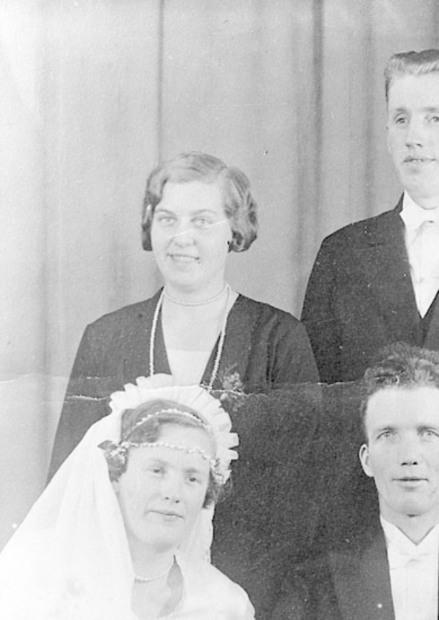 Ein Schwarz-Weiß-Foto einer Frau in einem Schleier, die zwischen zwei Männern steht, mit einem Vorhang dahinter, der einen Hochzeitstag suggeriert.