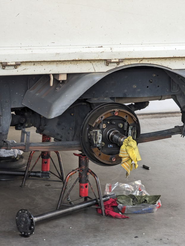 Ein gelber Stoff \c3cre einem in einer Garage geparkten Lkw drapiert, mit Werkzeugen und Gegenst\c3\a4nden, die vor ihm auf dem Boden verstreut sind.