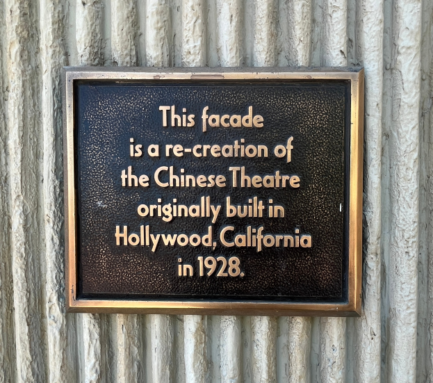 Schwarzes rechteckiges Schild mit weißer fettgedruckter Schrift, das die Fassade als Nachbildung des 1928er Chinesischen Theaters in Hollywood bezeichnet.