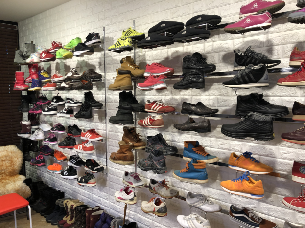 Ein Schuhgeschäft mit verschiedenen Arten von Schuhen auf Gestellen, einem Stuhl mit einem Teddybär auf der linken Seite und einer Wand im Hintergrund.