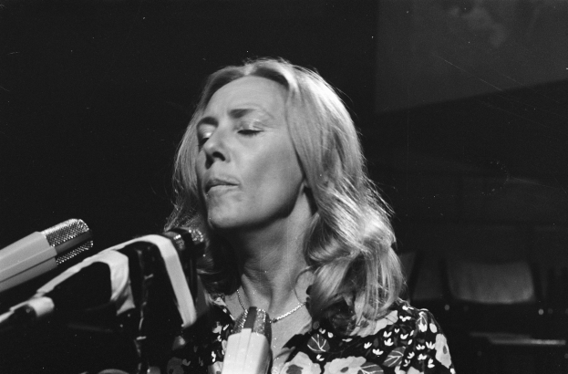 Eine Frau in einem schwarzen und weißen Outfit singt leidenschaftlich in ein Mikrofon, ihre Augen sind geschlossen und ihre Haare sind in einem klassischen Bob gestylt.