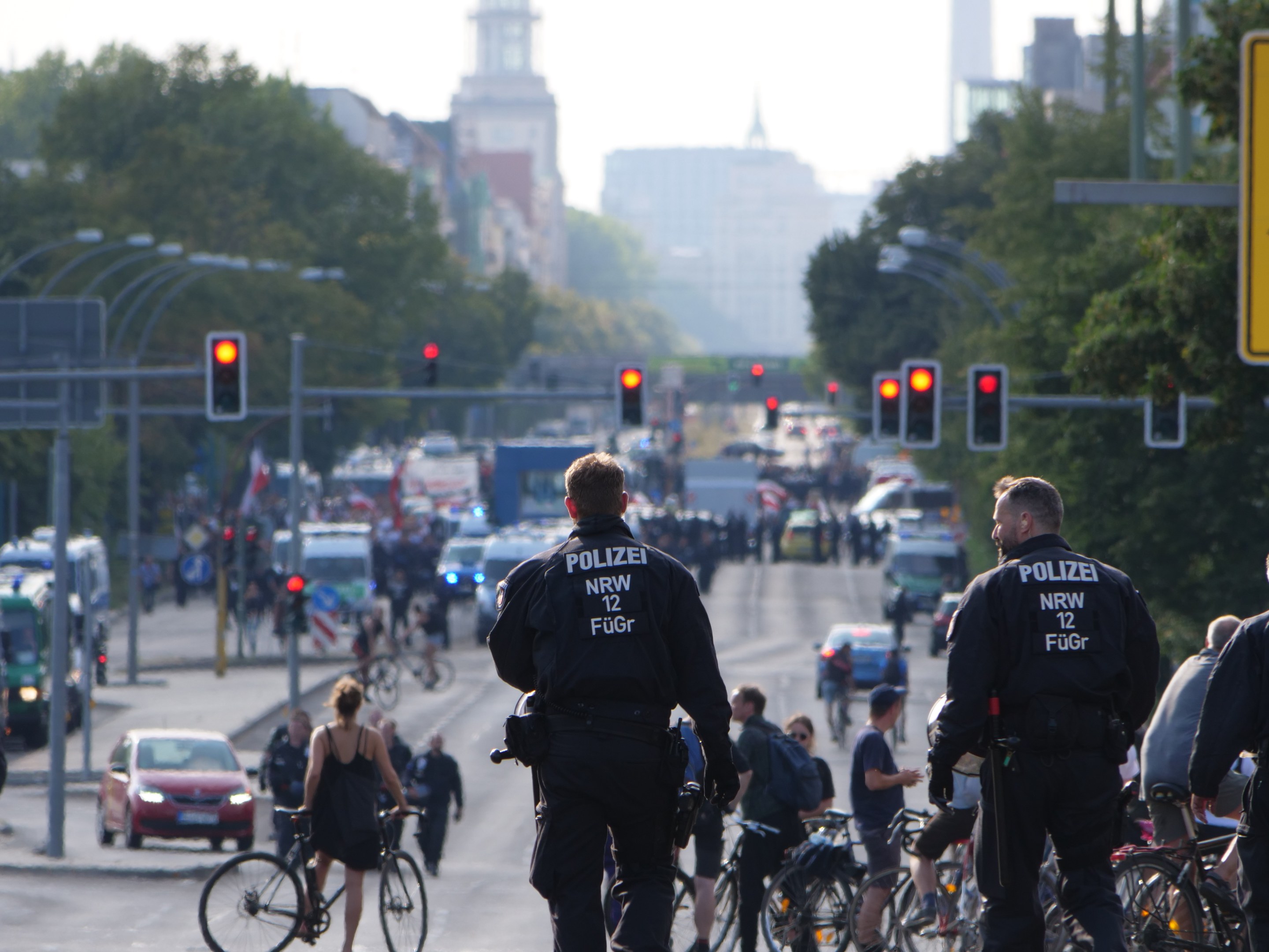 Polizeibeamte fahren mit Fahrrädern eine straße mit Bäumen und einem klaren blauen Himmel im Hintergrund entlang.