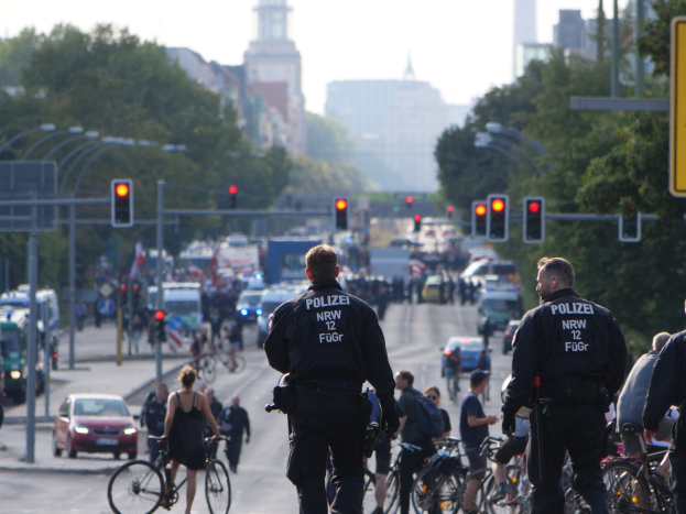 Polizeibeamte fahren mit Fahrrädern eine straße mit Bäumen und einem klaren blauen Himmel im Hintergrund entlang.