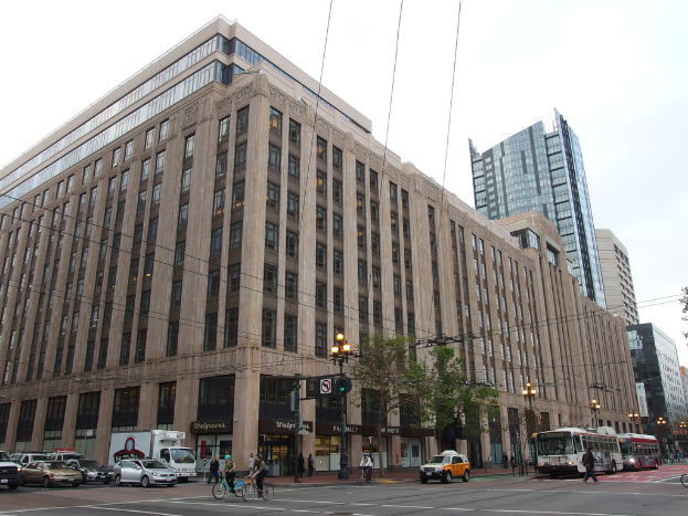 Eine Straße mit Menschen auf Fahrrädern, Bussen und Autos, mit Gebäuden, Bäumen, Laternen, Pfählen und Drähten im Hintergrund unter einem Himmel.
