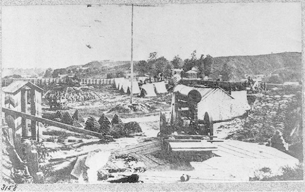 Ein Schwarz-Weiß-Foto einer Baustelle in San Francisco, Kalifornien, mit einer Maschine im Vordergrund, umgeben von Baracken, Bäumen, Hügeln und Himmel im Hintergrund, und Text unten, der besagt: "Die Baustelle einer neuen Brücke in der Stadt San Francisco, Kalifornien".