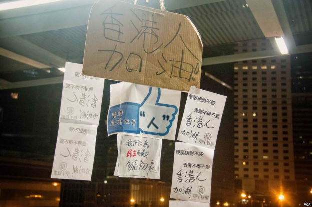 Gruppe von Menschen vor einem beleuchteten Gebäude an einem dunklen Ort mit Protestschildern an der Decke.