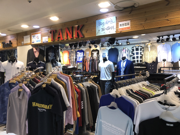 Ein modernes Bekleidungsgeschäft mit zahlreichen Shirts an den Wänden, Schaufensterpuppen in aktuellen Outfits, Texttafeln an den Wänden und Deckenbeleuchtung.