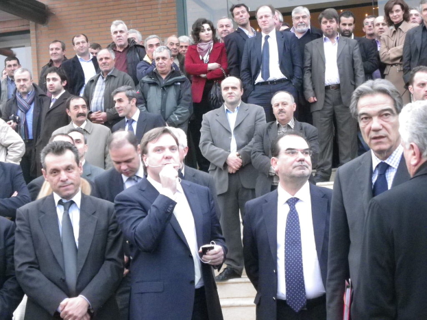 Eine Gruppe von Menschen, die zusammenstehen, einige in Anzügen, mit einer Backsteinwand im Hintergrund.