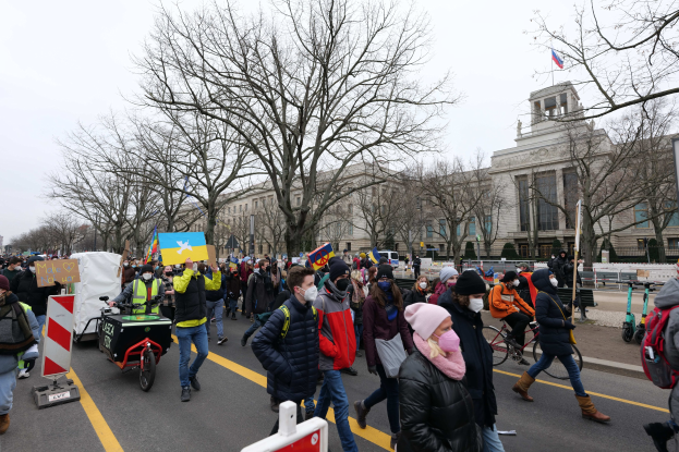 Eine große Gruppe von Menschen nimmt an einer Protestdemo in Washington, D.C. am 21. Januar 2020 teil und marschiert eine Straße entlang mit Plakaten, Schildern und Fahrrädern vor einer Kulisse aus Schildern, Bäumen und einem klaren blauen Himmel.